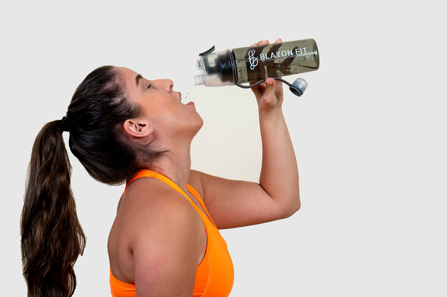 woman drinking from gym water bottle that can spray water also for refreshment
